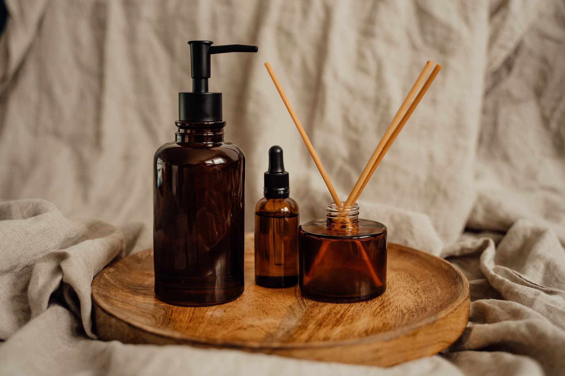 Amber and clear fragrance bottles on a linen surface with dried botanicals